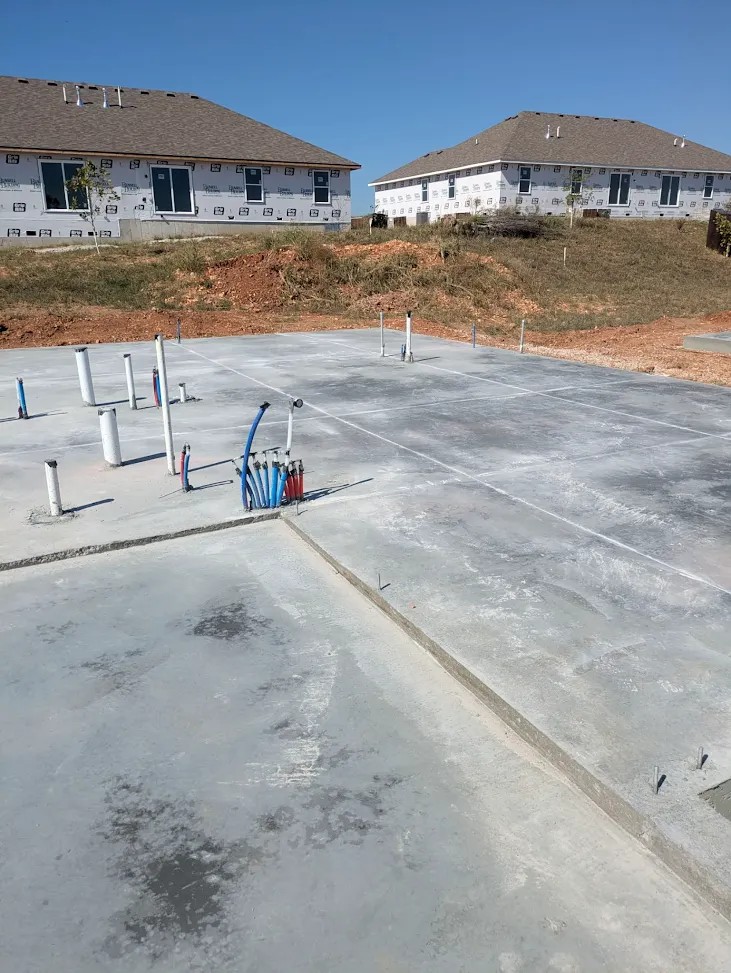 Concrete foundation slab with plumbing and water lines beside neighboring new homes Concrete foundation slab with plumbing and water lines beside neighboring new homes